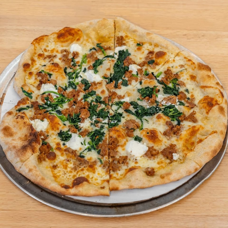 Pizza 54's white pizza with sausage, spinach, and ricotta cheese on a metal tray.