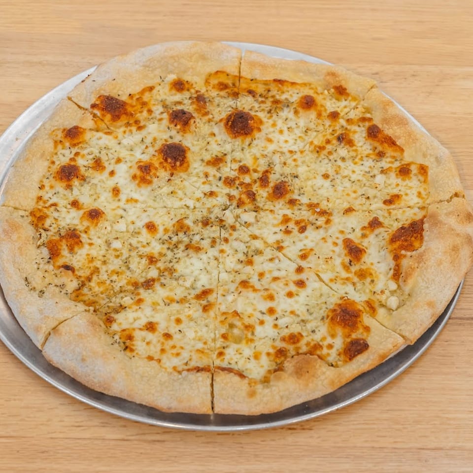 A whole white pizza from Pizza 54, topped with melted cheese and herbs, sliced on a metal tray.