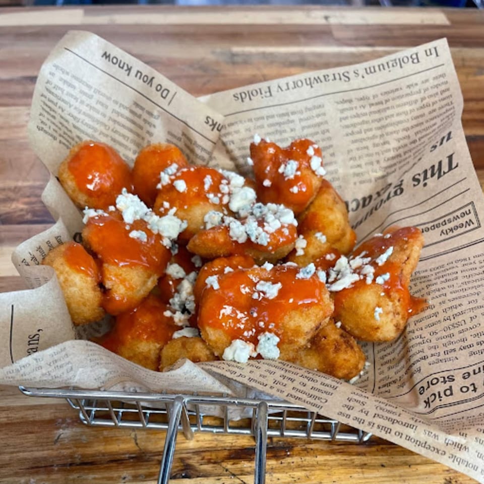 Pizza 54's crispy boneless wings coated in buffalo sauce and crumbled blue cheese, served in a metal basket.