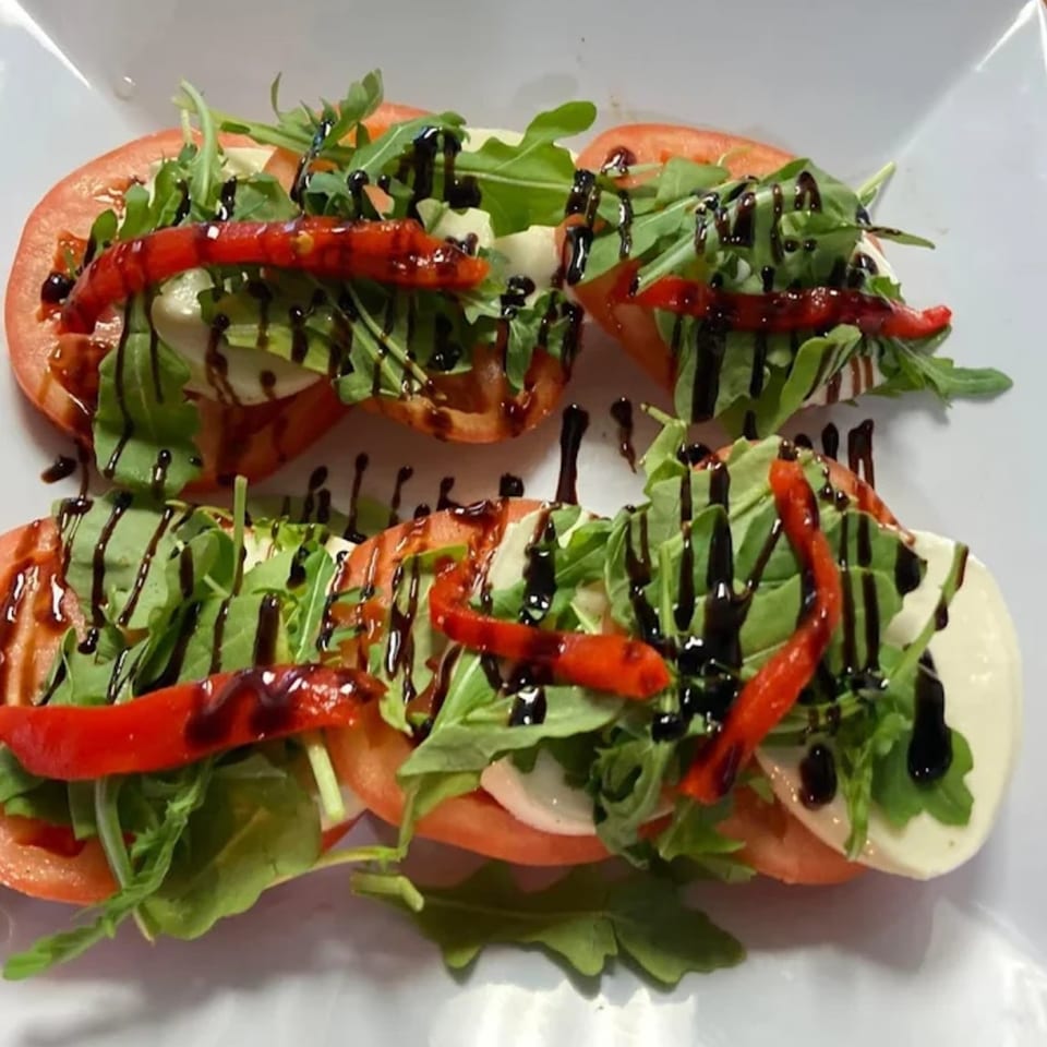 Two rows of Caprese salad with tomatoes, mozzarella, arugula, roasted red peppers, and balsamic glaze.
