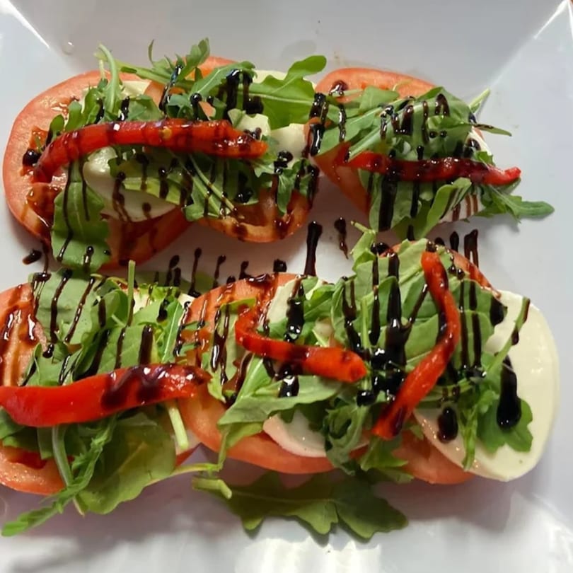 Two rows of Caprese salad with tomatoes, mozzarella, arugula, roasted red peppers, and balsamic glaze.