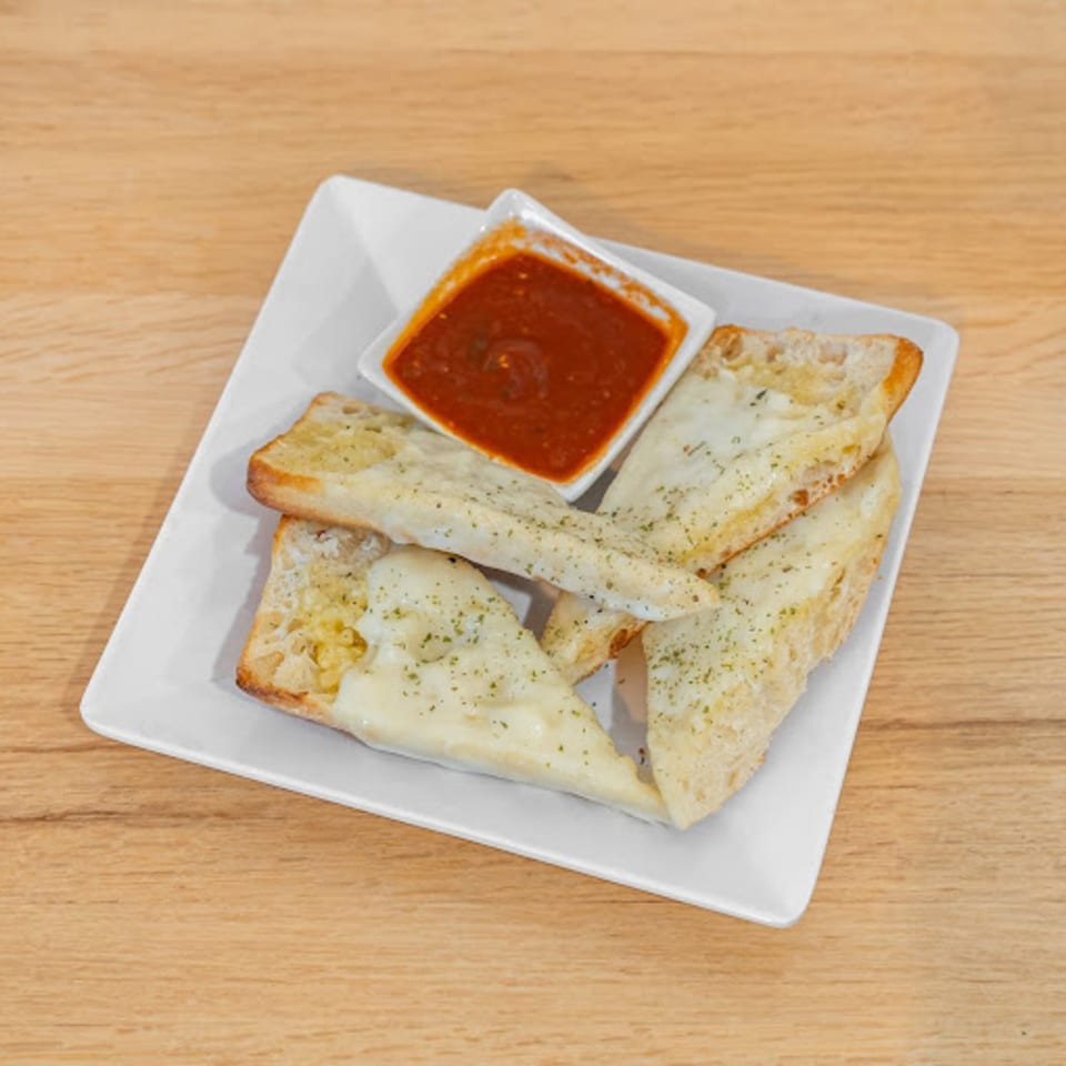 Cheesy garlic breadsticks with herbs and a side of marinara sauce on a white plate.