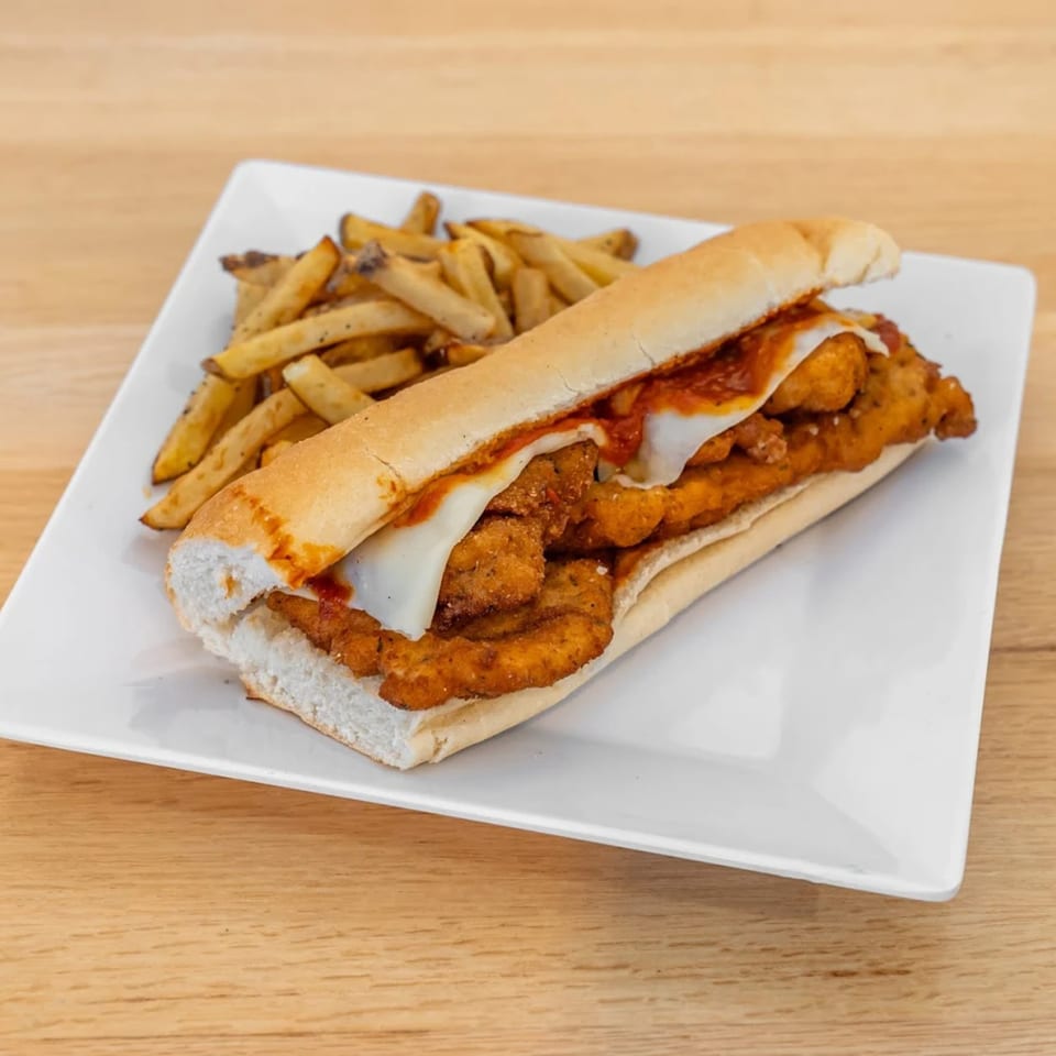 Chicken parmesan sub with melted cheese and marinara sauce, served with a side of fries.