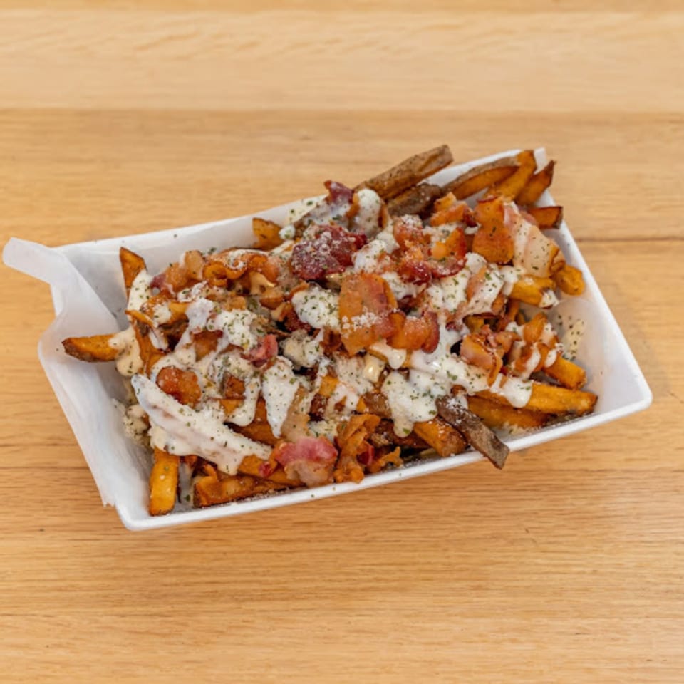 Sweet potato fries topped with bacon, white sauce, and seasoning in a white dish.