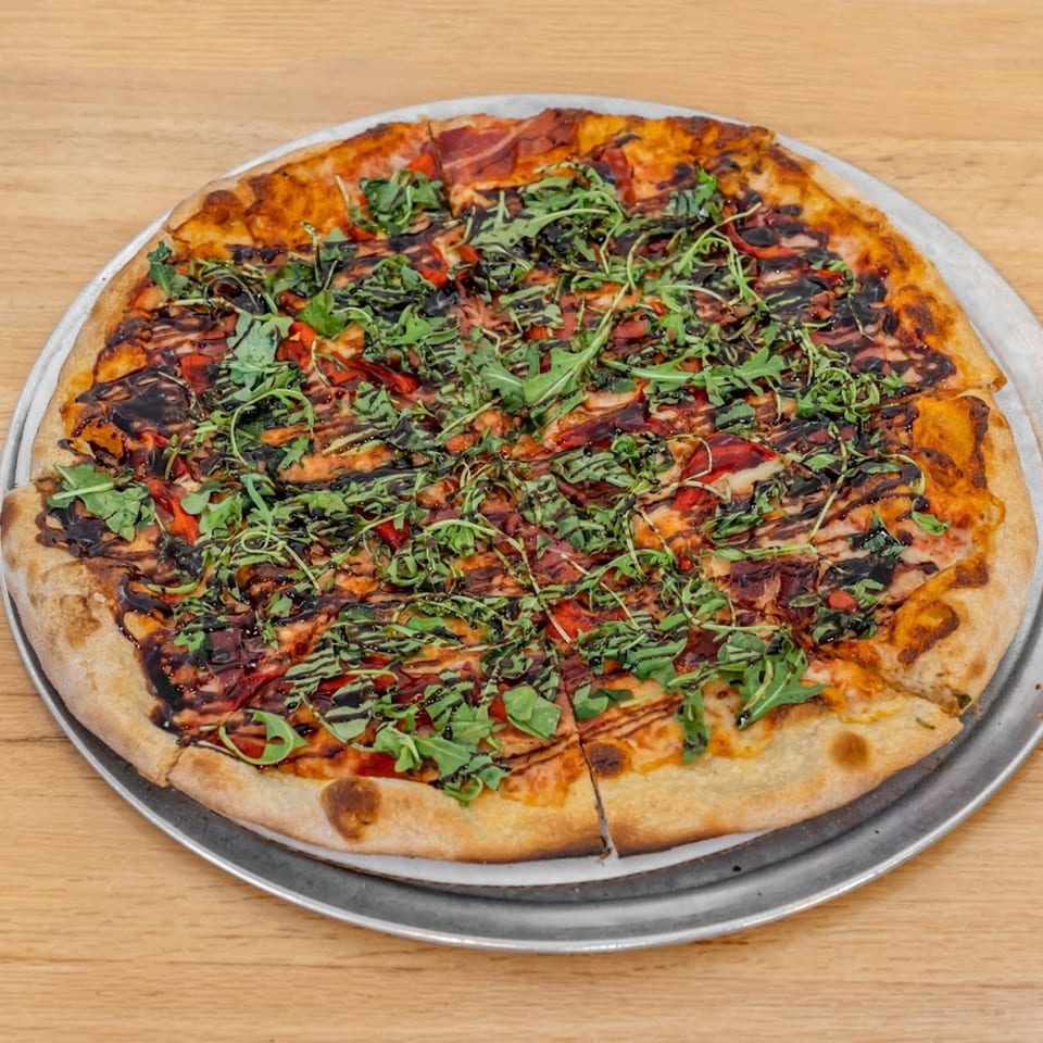 A whole Pizza 54 pizza, topped with arugula, red peppers, and a balsamic glaze.